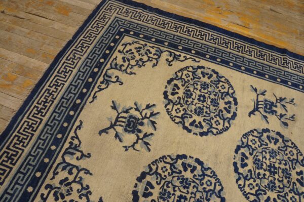 Cream and blue rug with floral medallions and greek key borders on peeling hardwood planks.