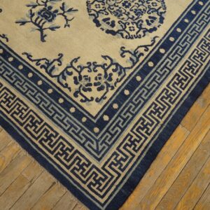 Cream rug with detailed indigo blue floral patterns and geometric meander borders on old wood plank flooring.