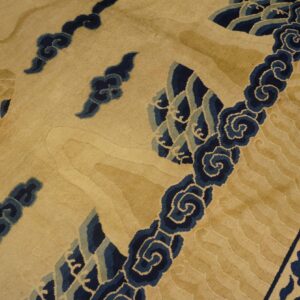 Tan and gold rug detail showing dark blue scrolling waves and a feathered wing design.