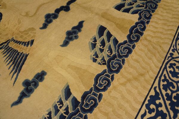 Tan and gold rug detail showing dark blue scrolling waves and a feathered wing design.