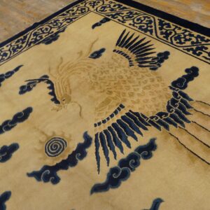 Tan rug with navy blue mythical bird and cloud patterns visible on light wood flooring.