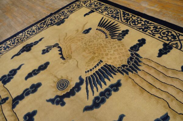 Tan rug with navy blue mythical bird and cloud patterns visible on light wood flooring.