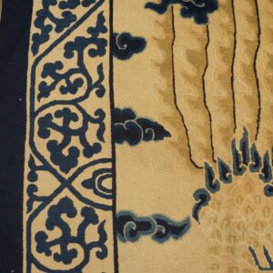 Close-up of a plush beige rug with a dark blue scrolling border next to rustic wooden planks.