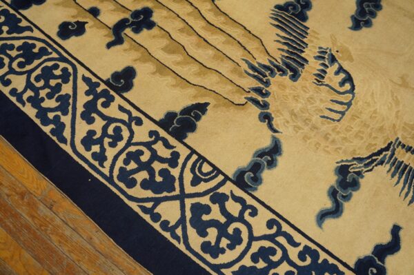 Low-pile rug in beige and navy blue features an ornate scrolled border and central stylized bird design on hardwood.