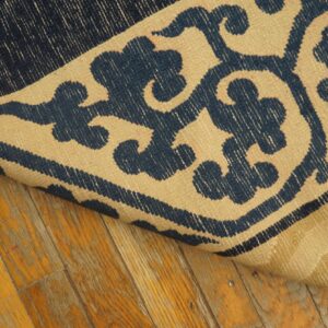 A flatwoven rug with a navy and beige scrolling pattern lies on distressed yellow wood floors.