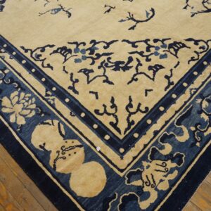 A closeup of a beige and indigo rug corner with elaborate floral borders on a worn hardwood floor.