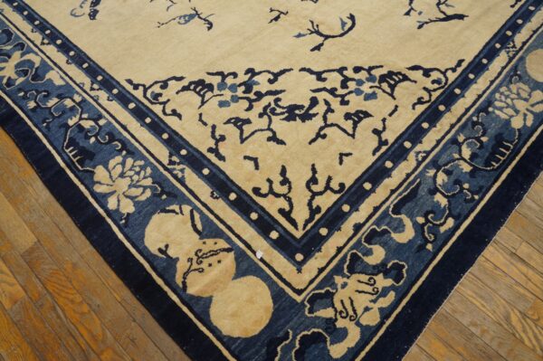 A closeup of a beige and indigo rug corner with elaborate floral borders on a worn hardwood floor.