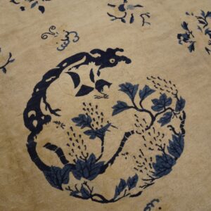 A close-up of a light beige rug featuring a dark blue central medallion with animal and vine motifs.