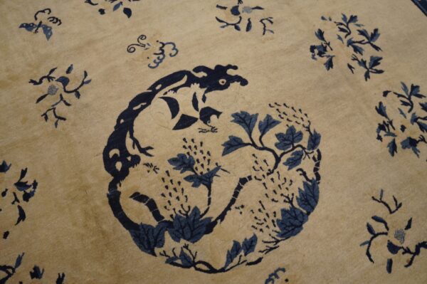 A close-up of a light beige rug featuring a dark blue central medallion with animal and vine motifs.