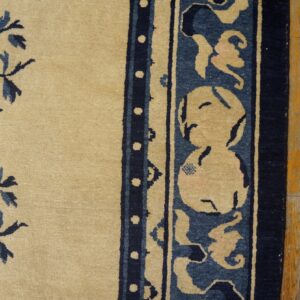 A tan rug with blue floral sprays and a detailed wide border lies on worn wooden flooring.