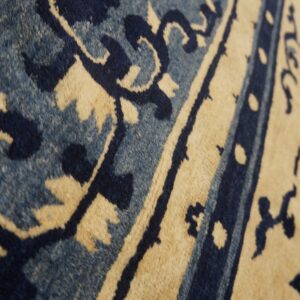 Close-up of a textured rug featuring floral motifs and borders in deep blue, light blue, and cream.
