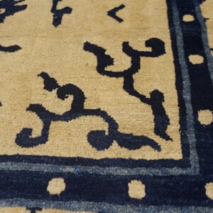Beige rug featuring a deep navy blue stylized pattern and a border accented with small tan dots.