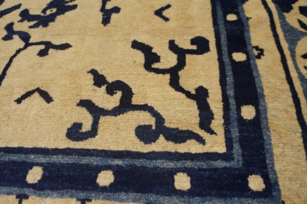 Beige rug featuring a deep navy blue stylized pattern and a border accented with small tan dots.
