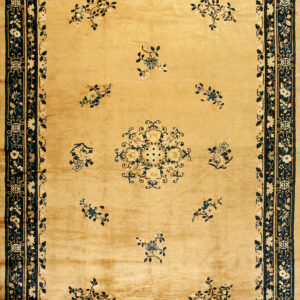 A rectangular golden rug displays blue floral motifs and a multi-band navy blue patterned border.