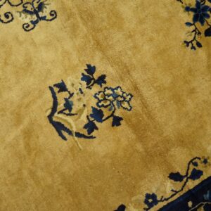 Detail shot of a gold rug with high pile and stylized navy and beige floral designs.