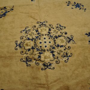 Tan rug texture showcasing blue and cream floral designs surrounding an ornate central motif.