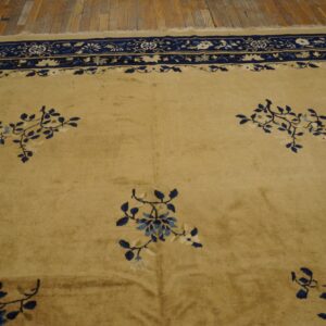 A tan rug with navy and cream ornate borders and scattered blue floral patterns rests on wood floors.