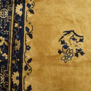 Gold rug detail showing a dense navy blue border with floral patterns and isolated blue motifs in the field.