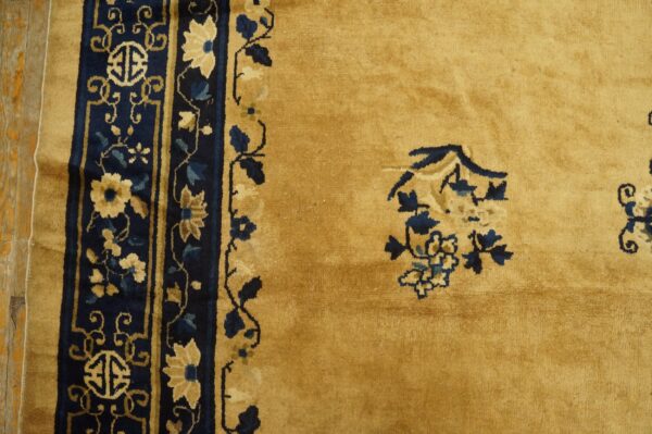 Gold rug detail showing a dense navy blue border with floral patterns and isolated blue motifs in the field.