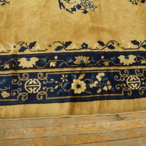 Golden yellow rug with a wide navy blue border featuring intricate light blue and tan floral patterns on wood flooring.
