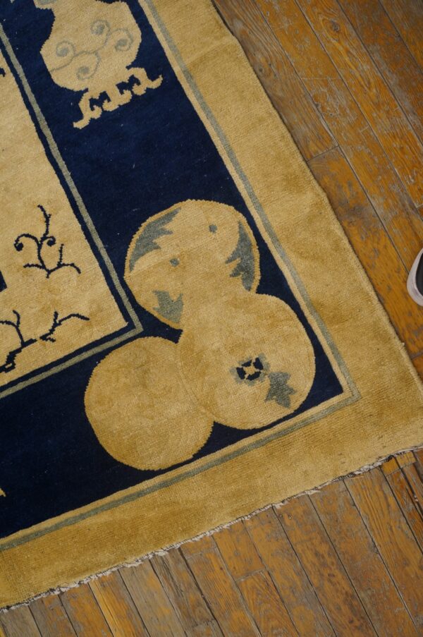 Stylized mustard yellow and navy blue rug featuring ornate patterns rests on distressed wood plank flooring.