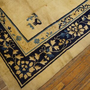 Diagonal view of a tan rug featuring navy blue and teal floral borders on rustic wooden floorboards.
