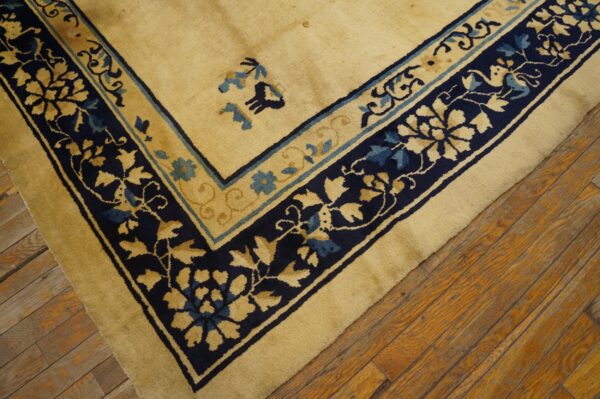 Diagonal view of a tan rug featuring navy blue and teal floral borders on rustic wooden floorboards.