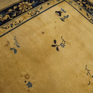 Yellow field rug with navy and gold floral border, scattered blue motifs, shown on light brown wood planks.