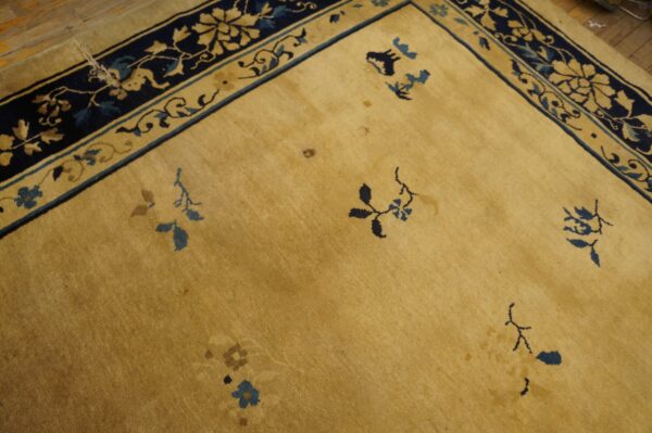Yellow field rug with navy and gold floral border, scattered blue motifs, shown on light brown wood planks.
