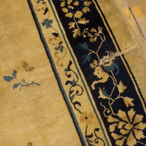 Golden rug with navy and tan border featuring blue accents on worn wood floor.