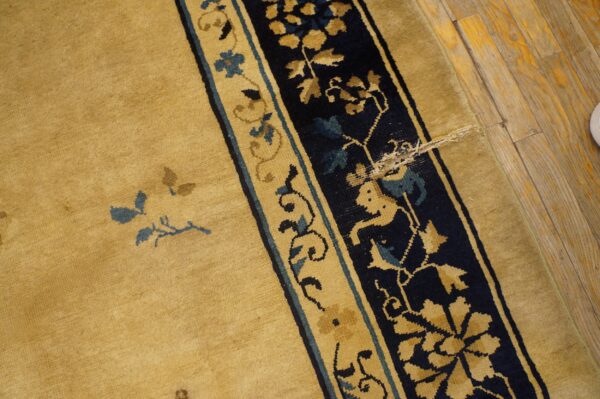 Golden rug with navy and tan border featuring blue accents on worn wood floor.