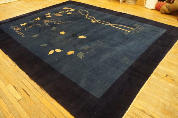 Dark blue rug featuring a vine, leaves, and grape pattern in tan and green, laid on light wood flooring.