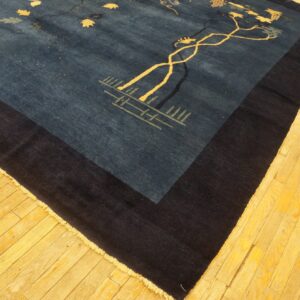 Deep blue rug with yellow vine patterns and a broad dark border, lying on rustic golden wood flooring.