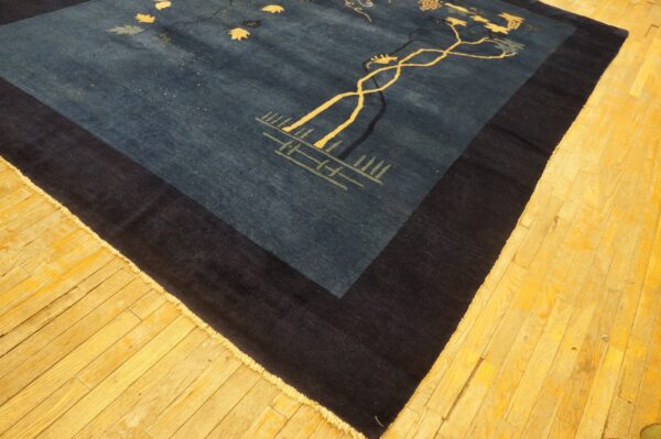 Deep blue rug with yellow vine patterns and a broad dark border, lying on rustic golden wood flooring.