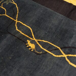 Dark blue rug featuring gold vines, yellow leaves, a small gold animal, and a dark border on wood flooring.