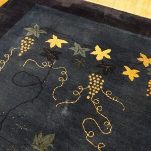 Dark blue rug with a gold, olive, and navy grapevine and leaf pattern rests on wooden floors.