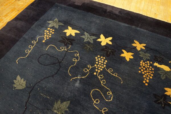Dark blue rug with a gold, olive, and navy grapevine and leaf pattern rests on wooden floors.