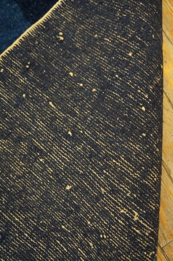 Detail of a rug underside showing dark blue weaving with light beige diagonal striations on wood flooring.
