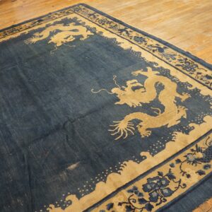 Low-pile indigo rug featuring large tan dragon motifs and a complex patterned border on hardwood floors.