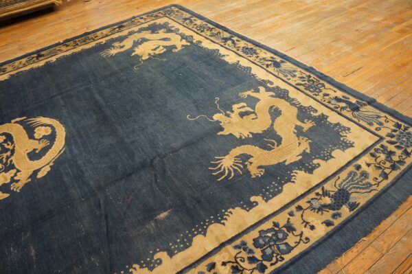 Low-pile indigo rug featuring large tan dragon motifs and a complex patterned border on hardwood floors.