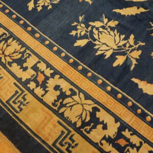 Diagonal view of a blue rug featuring gold floral motifs and detailed geometric borders on wood flooring.