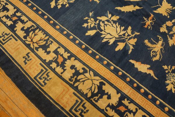 Diagonal view of a blue rug featuring gold floral motifs and detailed geometric borders on wood flooring.
