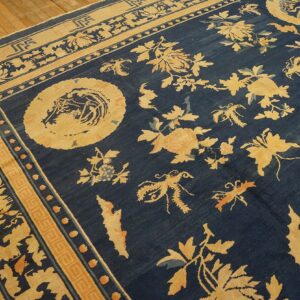 Deep blue rug with elaborate tan and orange floral patterns and borders resting on wood plank flooring.