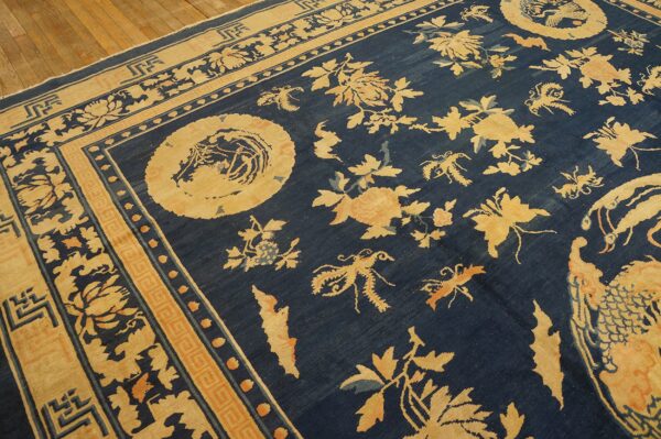 Deep blue rug with elaborate tan and orange floral patterns and borders resting on wood plank flooring.