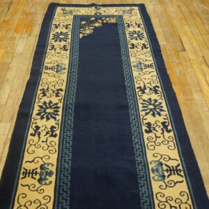Navy blue runner rug with cream borders featuring floral and geometric patterns, displayed on worn wooden flooring.