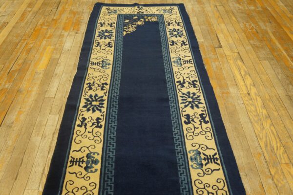 Navy blue runner rug with cream borders featuring floral and geometric patterns, displayed on worn wooden flooring.