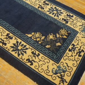 Navy blue rug featuring yellow and teal floral and geometric borders rests on light-toned wooden floorboards.