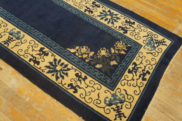 Navy blue rug featuring yellow and teal floral and geometric borders rests on light-toned wooden floorboards.