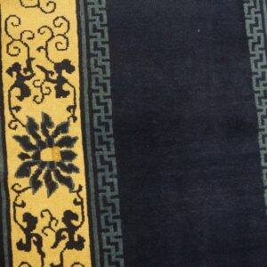 A navy and yellow rug with floral motifs and geometric borders rests on light wood planks.