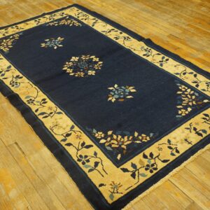 Navy blue rug with a gold floral border rests on a distressed golden hardwood floor.